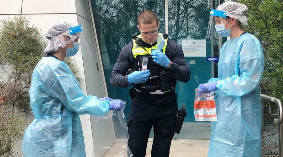 Health workers collect saliva sample from Victoria Police Officer for saliva test pilot